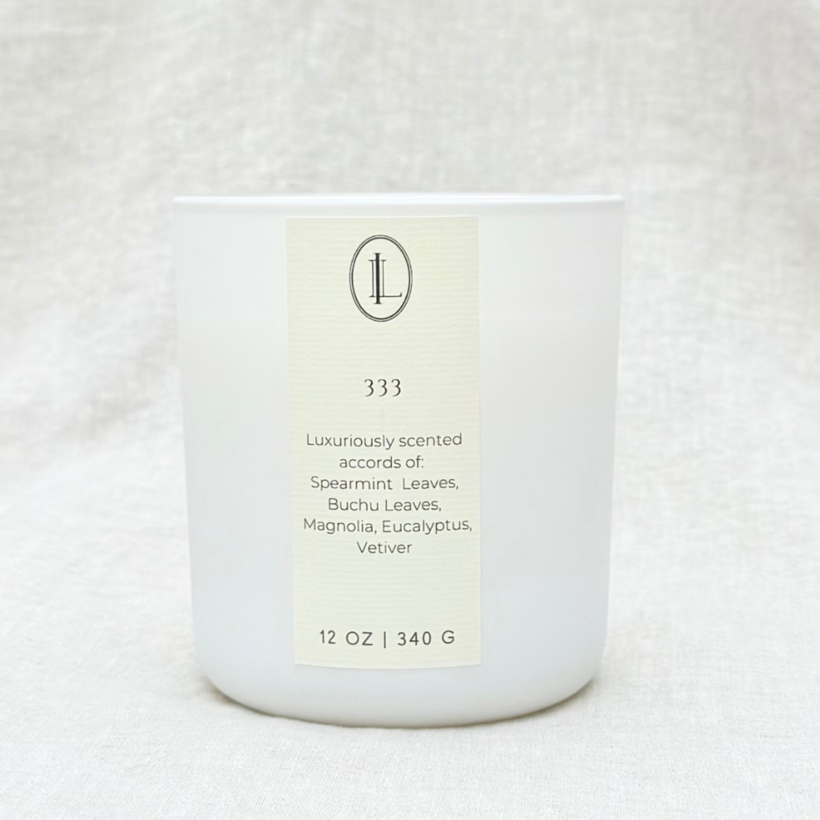 Eucalyptus and mint candle with label that reads angel number 333 on a matte white glass vessel