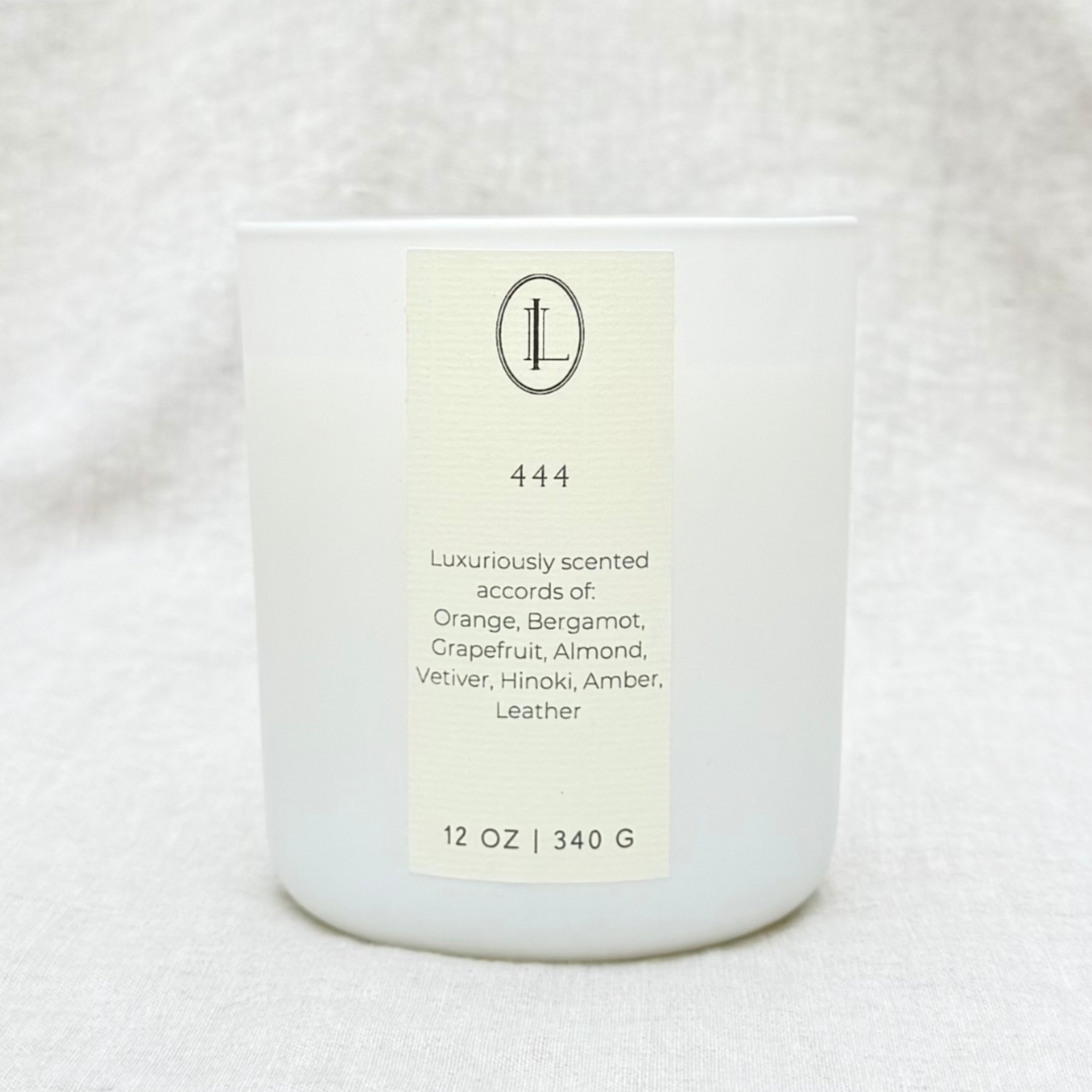 A citrus, leather, amber scented wood wick candle with a label that reads angel number 444 in a matte white glass vessel