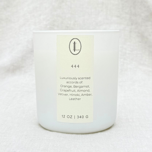 A citrus, leather, amber scented wood wick candle with a label that reads angel number 444 in a matte white glass vessel