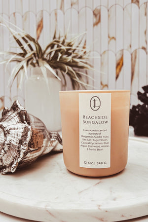 Beachside Bungalow 12 oz wooden wick candle in a matte sand glass candle vessel scented with bergamot, yuzu, sea salt, sage flower, coastal cyclamen, blue algae, driftwood, amber, & tonka bean.