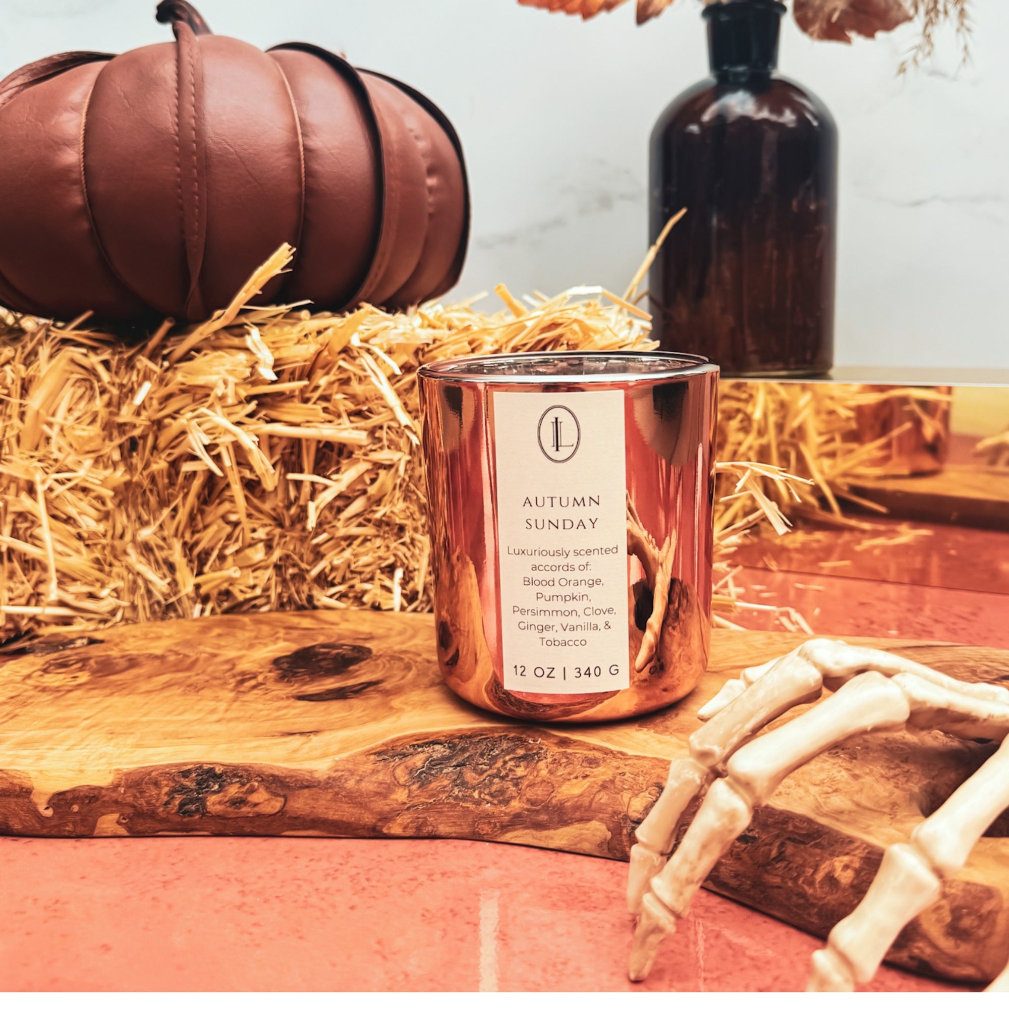 woodwick Candle labeled 'Autumn Sunday' on a wooden surface with pumpkins and hay in the background