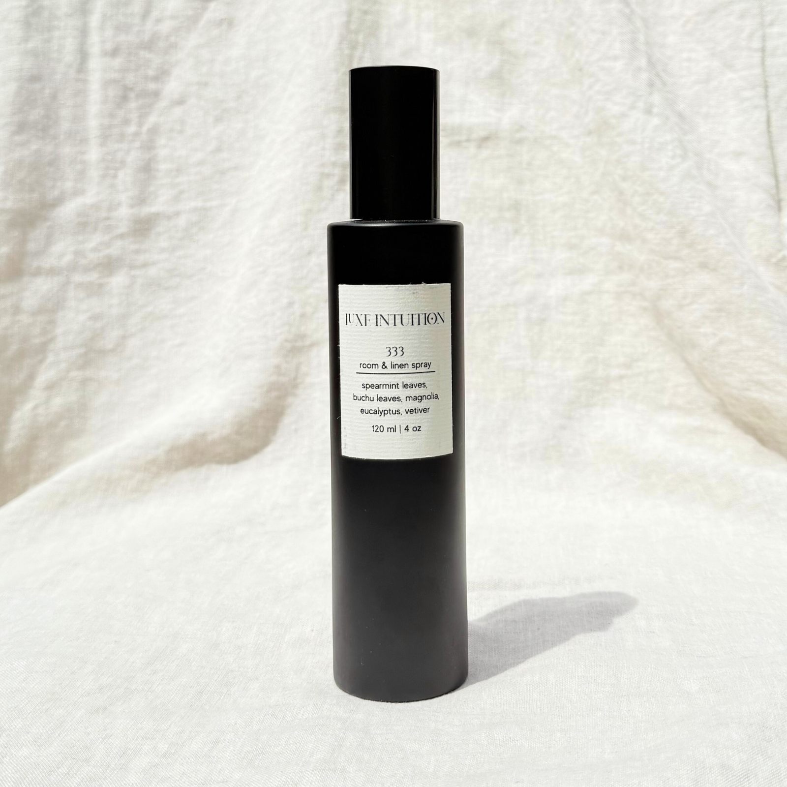 spearmint and eucalyptus scented room & linen spray in a black spray bottle resting on a linen background