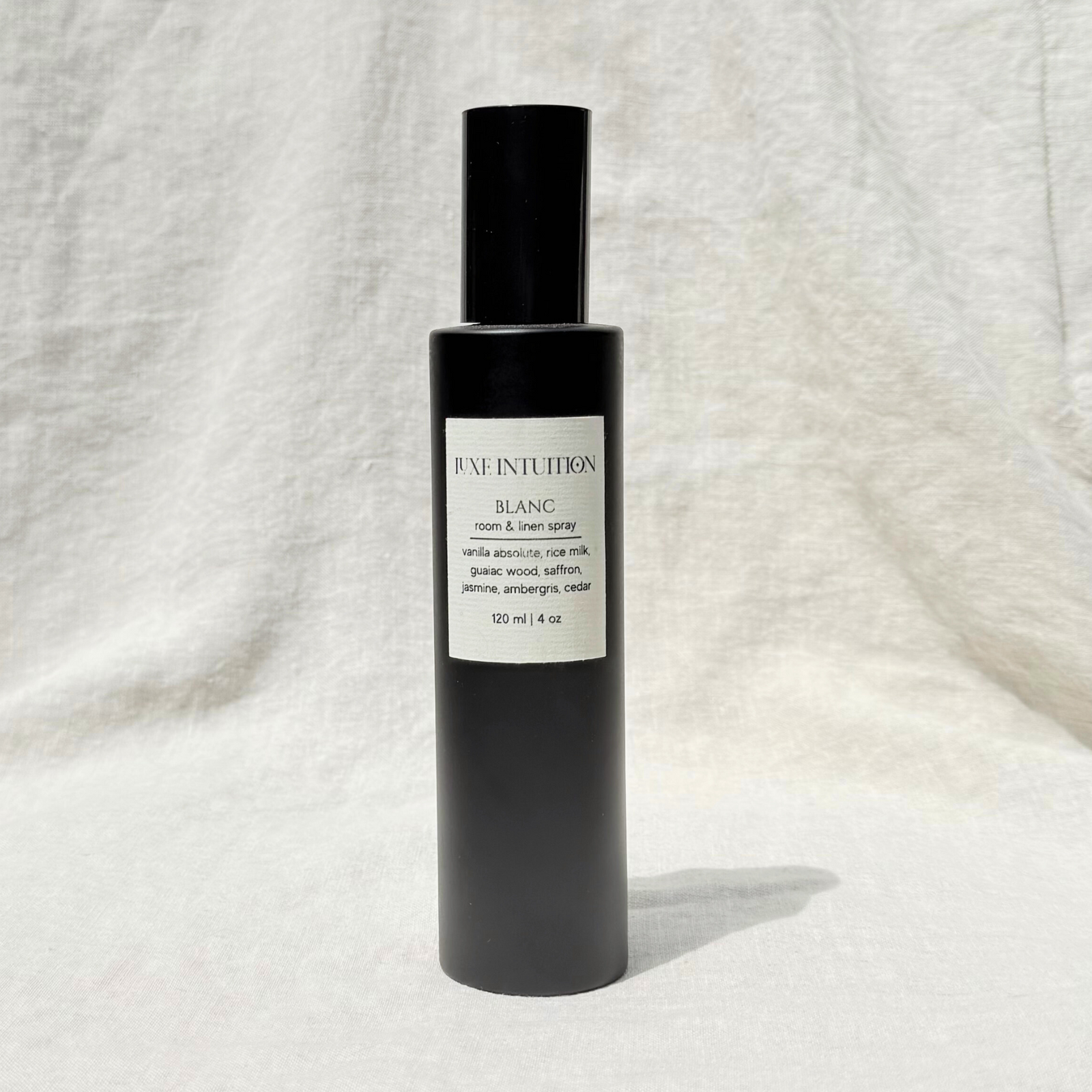 Soft vanilla scented room & linen spray in a black spray bottle resting on a linen background