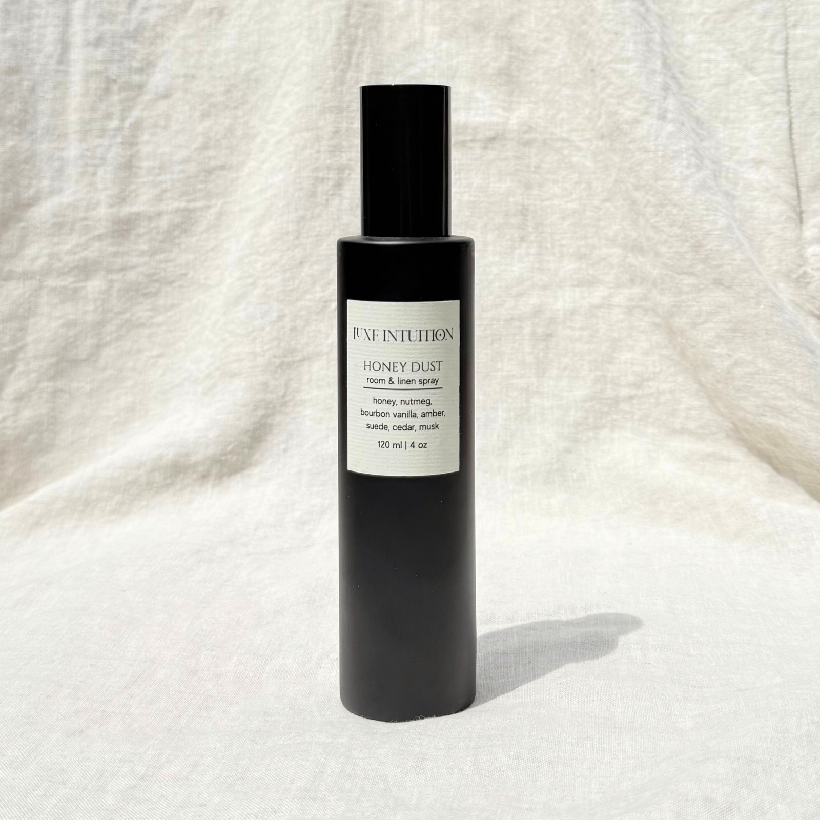 Honey scented room & linen spray in a black spray bottle resting on a linen background