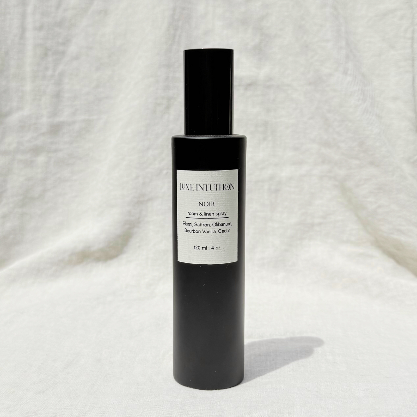 Vanilla scented room & linen spray in a black spray bottle resting on a linen background