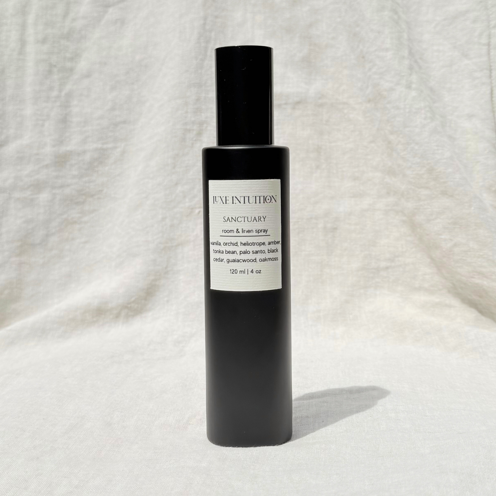 Palo Santo Scented Room And Linen Spray In A Black Bottle Labeled Sanctuary on a linen background.