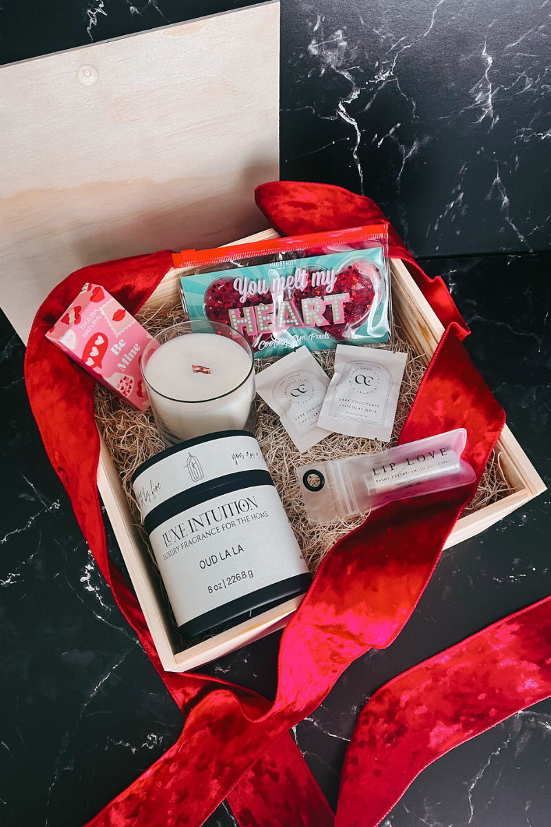 Image of opened luxe love box with oud la la candle, shower steamers, lip love chapstick, heart shaped chocolates, and a set of heart shaped cooling eye pads