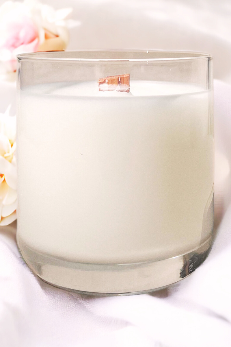 la luna candle in clear glass jar sitting on white blanket with white flowers 